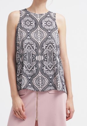 Haut sans manches au motif noir et blanc, avec des détails ornés et un col arrondi, associé à une jupe rose clair.