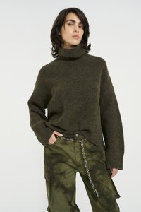 Alyvuogių spalvos turtleneck megztinis su tekstūruotu raštu ir guma apkaustais, derinamas su žaliais cargo džinsais su ryškiu spalvų perėjimu ir grandine.