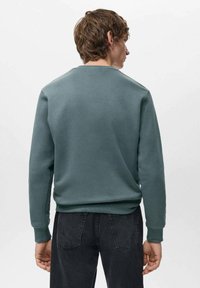 Felpa verde con scollo rotondo e polsini a costine, realizzata in tessuto morbido, vista da dietro, abbinata a jeans neri.