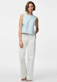 Svijetloplava, kvadratična bezrukavna majica s okruglim izrezom uparena s visokim bijelim širokim trapericama i ravnim sandalama.