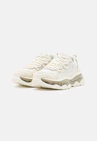 Jasnobeżowe sneakersy z siateczkową i syntetyczną cholewką, wyposażone w amortyzowaną podeszwę, teksturowane detale oraz przezroczystą środkową część podeszwy.