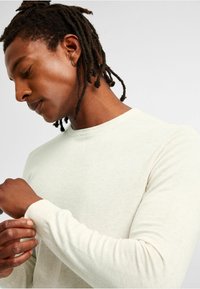Lichtgrijze sweatshirt met lange mouwen en ronde hals, met een aansluitend ontwerp en ribbelmanchetten. Gladde textuur met subtiele stikseldetails.