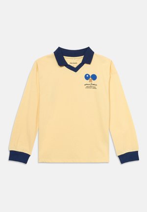Koszulka polo z długim rękawem w jasnym żółtym kolorze z granatowym kołnierzykiem i mankietami, z niebieskim logo rakietek do tenisa stołowego oraz napisem "Mini Rodini" na piersi.