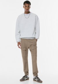 Siv sweatshirt z nizkimi rameni, rjave cargo hlače z več žepi in nizki športni čevlji v sivih in zelenih odtenkih.