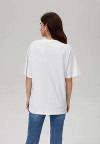Hvit kortermet t-skjorte med avslappet passform og rund hals, laget av myk bomull. Kombinert med blå denim jeans, sett fra baksiden.