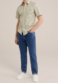 Krátký rukáv, světle zelená košile s květinovým vzorem, v kombinaci s modrými rovnými džínami a bílými teniskami. Košile s knoflíky a límečkem.