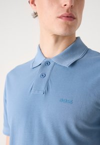 Világoskék polo póló struktúrált anyagból, klasszikus gallérral, két gombbal és egy kicsi hímzett "BOSS" logóval a mellkasán.