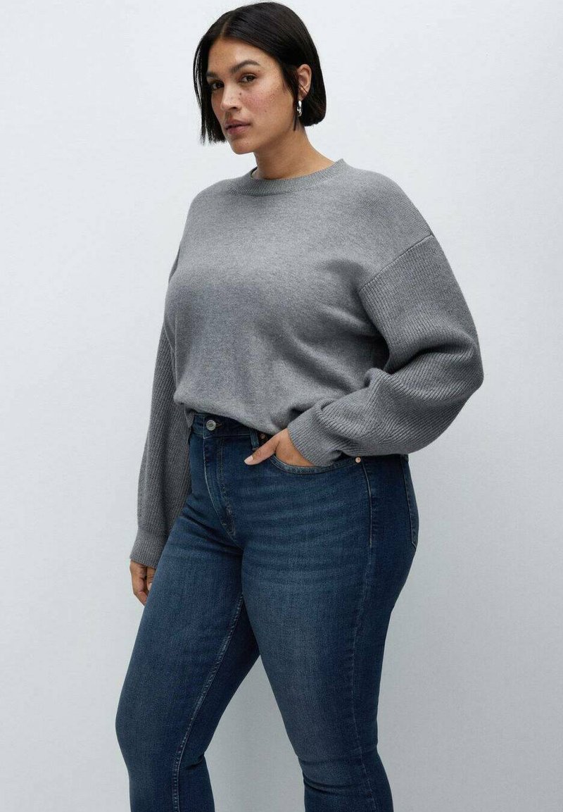 Grauer Strickpullover mit rundem Ausschnitt und gerippten Ärmeldetails, kombiniert mit dunkelblauen, eng anliegenden Jeans. Glatte Textur und lässige Passform.