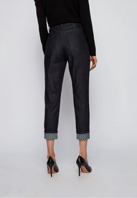 Jeans índigo oscuros con puños doblados que presentan un borde estampado, bolsillos traseros y un corte recto; combinados con zapatos de tacón alto negros.