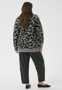 Grauer Leopardenmuster-Pullover mit langen Ärmeln und geripptem Saum. Kombiniert mit schwarzen Fake-Leder-Hosen und schwarzen flachen Schuhen.