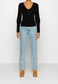 Haut noir à manches longues côtelé avec un col en V et des accents de boutons ; associé à un jean à jambes larges bleu clair et des bottes à talons carrés beiges.