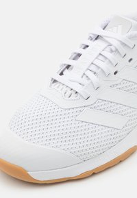 Witte sportieve schoen met een ademende mesh bovenkant, drie duidelijke strepen, rubberen zool en gestructureerde accenten. Vetersluiting met demping.
