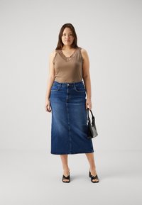 Brun bluseløs topp med blonder, sammen med et langt blått jeansskjørt. Modellen bærer en liten svart håndveske og har på seg svarte hælsandaler.