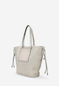 Bolso de Tote en material tejido de color gris claro con un parche rectangular liso y acentos de tachuelas. Cuenta con dos asas largas y lazos laterales ajustables.