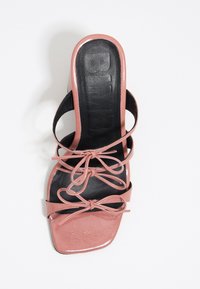 Sandale à talon ouvert rose avec des brides, bout carré, trois nœuds et semelle intérieure rembourrée noire sur fond blanc.