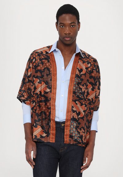 Kimono-stijl blouse van een donkere stof met complexe patronen in oranje, bruin en teal. Heeft een open voorkant en korte mouwen. Blauwe shirt eronder.