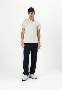Lys grå polo shirt med sorte accenter, parret med navy sweatpants og grå sneakers. Modellen bærer en sort kasket. Casual outfit.