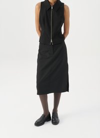 Μαύρη αμάνικη μπλούζα με γιακά και μπροστινό φερμουάρ, συνδυασμέ�νη με μια μακριά μαύρη φούστα. Συμπληρωμένη με μαύρες καστόρινο παπουτσιές και καφέ καλσόν.