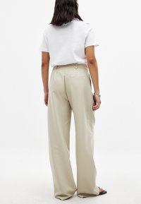 Gai bēšas platās bikses ar gludu tekstūru un aizmugurējo kabatu. Kombinētas ar vienkāršu baltu krekli ar īsām piedurknēm.