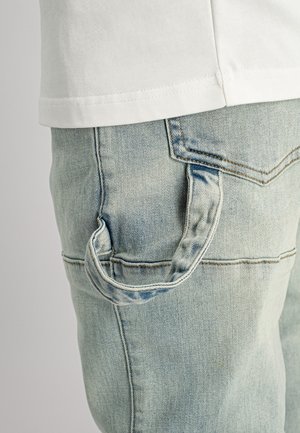 Lichtblauwe spijkerbroek met een zijzak en een lus. De stof heeft een vervaagde textuur met zichtbare stiksel-details.