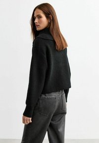 Svart stickad tröja med ribbad polokrage, kort design och texturerad tyg, kombinerad med högmidjade grå byxor.