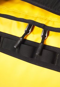 Bolsa impermeable amarilla con cierre de cremallera negra, que cuenta con un cordón ajustable y un hardware texturizado para un mejor agarre. Correa plana para un cierre seguro.