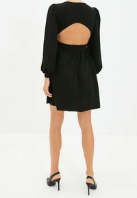 Czarna sukienka z bufiastymi rękawami, dopasowaną talią i odkrytymi plecami. Materiał wydaje się gładki, o skromnej długości powyżej kolana.