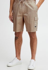 Beige cargoshorts lavet af bomuld med elastik i taljen, snørejustering, sidelommer og en lomme med klap på låret.