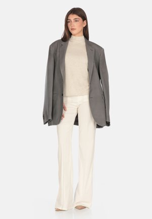 Grauer übergroßer Blazer über einem cremefarbenen Stehkragenoberteil, kombiniert mit weißen Schlaghosen und beigen Absätzen, die glatte Texturen und maßgeschneidertes Design aufweisen.