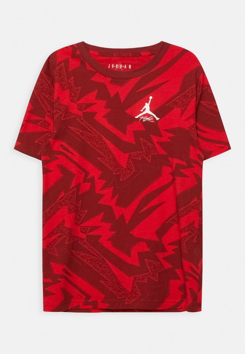 Červené tričko s krátkým rukávem vyrobené z měkké látky, zdobené výrazným zigzagovým vzorem ve tmavších odstínech červené, s bílým logem Jordan na hrudi.