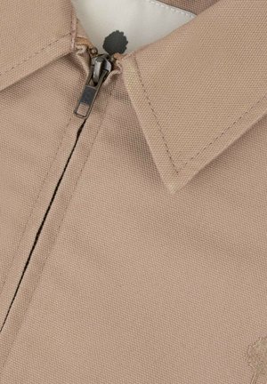 Giacca in tessuto beige con cerniera parzialmente chiusa, che mostra il colletto e la parte superiore del petto.