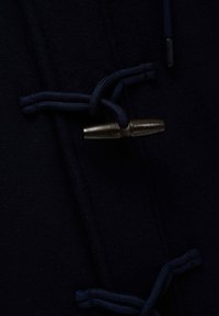 Abrigo de lana azul marino con cierres tipo toggle, cordones azul oscuro y acentos metálicos, que muestra una textura suave y un diseño elegante.