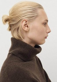 De bruine coltrui heeft een geribbeld textuur. Het haar is gestyled in een lage bun, met een gladde, rechte silhouet vanuit het profiel bekeken.