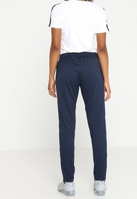 Marinblå idrottsbyxor med elastisk midja, avsmalnande ben och sidostänger i kontrastfärg. Matching med en vit kortärmad topp och grå skor.