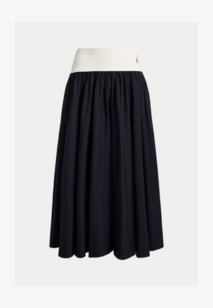 Φούστα μέχρι το γόνατο από σκούρο μπλε ύφασμα με λευκή ελαστική ζώνη στη μέση. Διαθέτει πιετέ σχέδιο και ένα μικρό κόκκινο λογότυπο ως λεπτομέρεια.