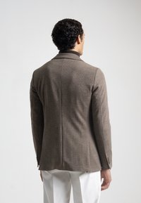Blazer de cuadros marrón con un corte entallado, hombros estructurados y un cuello con muesca, que presenta una textura sutil y dos botones en los puños.