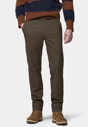Mann trägt braune Slim-Fit-Hose, braunen Ledergürtel, braune Schnürstiefel und einen braun-navy gestreiften Pullover mit den Händen in den Taschen.