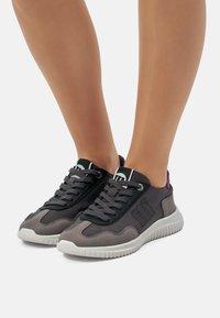 Zapatillas grises con detalles negros y patrones texturizados, que cuentan con una suela flexible, un diseño de cordones y un pequeño detalle púrpura en el talón.