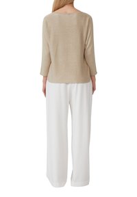 Beige Strickpullover mit Dreiviertelärmeln, rundem Ausschnitt und weicher Textur; kombiniert mit weißen, lockeren Hosen.