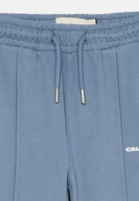 Γαλάζιο κοντό παντελόνι φόρμας με ελαστική μέση, κορδόνι και ασημένια μεταλλικά στοιχεία. Διαθέτει διακριτική κατακόρυφη ραφή και λογότυπο σε λευκό χρώμα.