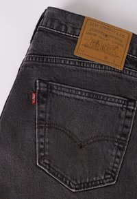 Poche arrière d'un jean Levi's noir avec coutures visibles, étiquette de marque rouge et étiquette en cuir marron Levi Strauss & Co. sur la ceinture.