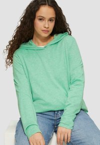 Hellgrüne Kapuzenjacke aus weichem Stoff, mit lässigem Schnitt, langen Ärmeln und Kordelzugkapuze. Getragen mit blauen Jeans.