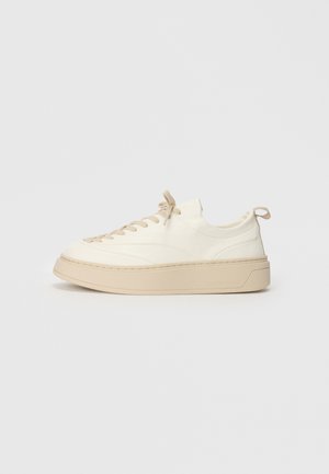 Vita lädersneakers med beige detaljer, med rund tå, platta snören, en tjock sula och en sydd detalj runt basen.