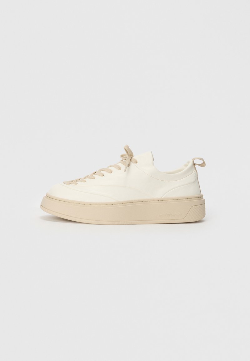 Sneakers de pele branca com detalhes em bege, apresentando um bico arredondado, atacadores planos, uma sola grossa e um detalhe cosido à volta da base.