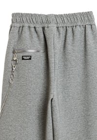 Pantalones de chándal grises con cintura elástica, bolsillo lateral con cremallera y detalle de cadena plateada. Fabricados con un tejido suave y texturizado.