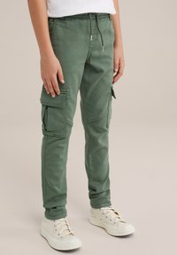 Zelene cargo hlače s slim fit krojem, ki imajo več velikih žepov, elastični pas z vrvico in gladko mešanico bombaža. Vključeni so tudi beli športni copati.