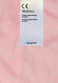 Rosa nätfabric med en slät textur, som har en vit vårdlapp med svart text som anger överensstämmelse och varningar.