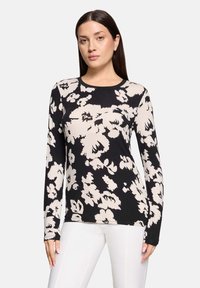 Czarna i beżowa bluzka z długim rękawem w kwiatowy wzór, z okrągłym dekoltem, abstrakcyjnymi wzorami kwiatów oraz dopasowanym krojem. Miękka tkanina o subtelnej teksturze.