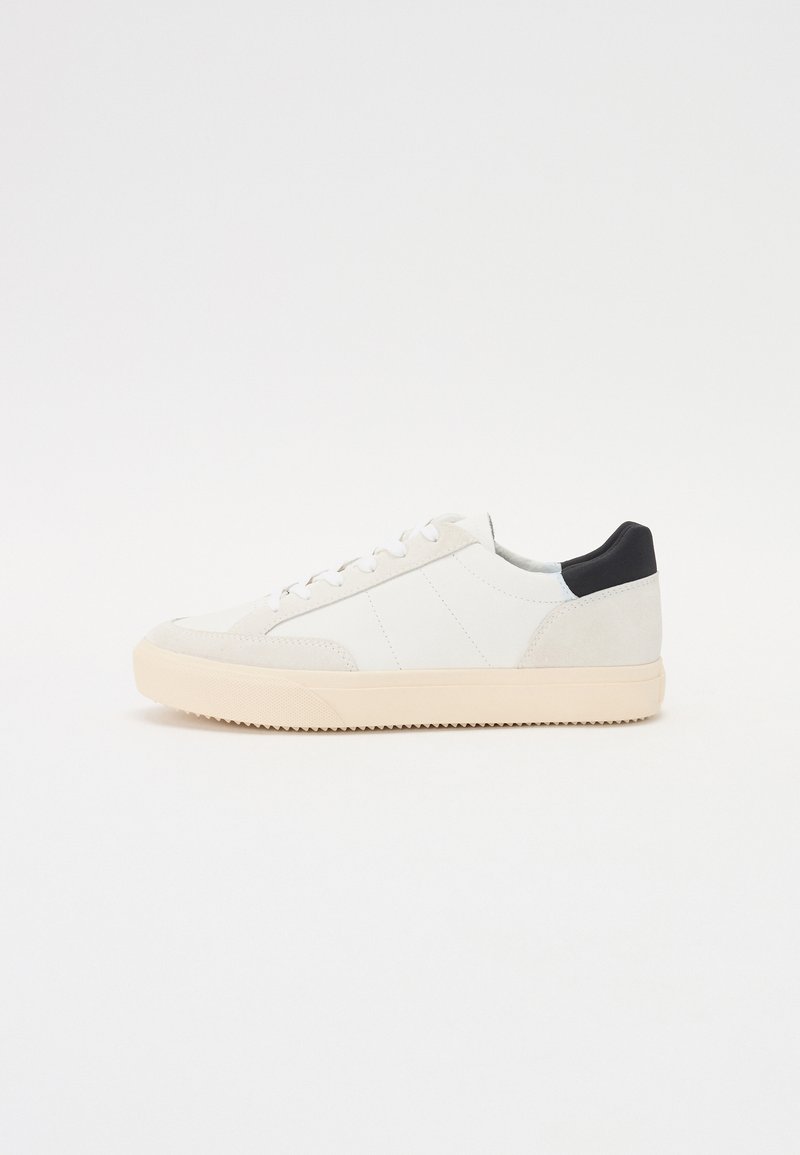 White leather sneaker with a textured suede toe, beige rubber sole, and a black heel accent. Features lace-up design and side panel stitching.