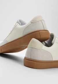 Baskets blanches avec un dessus en cuir suédé texturé et en cuir lisse, présentant une semelle en caoutchouc beige et des détails de couture minimaux.